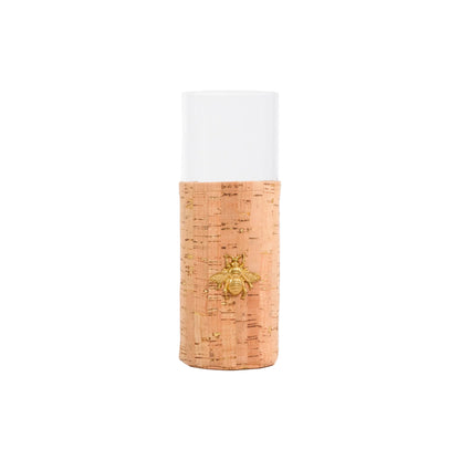A cylindrical glass container with a natural cork textured lower half and a white frosted upper half, featuring a small gold bee ornament on the front.